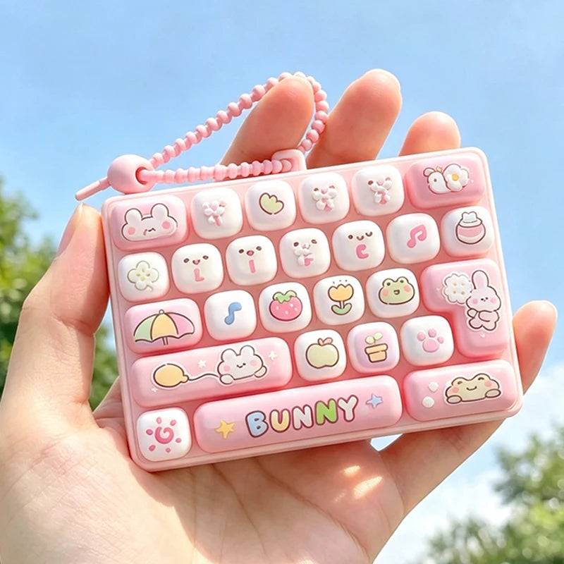 A hand holds a pink keycap fidget keychain featuring various cute cartoon-themed buttons and keys.