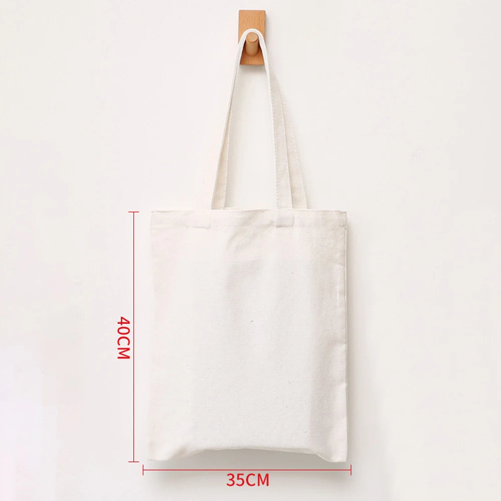 A white reusable canvas shopping tote bag hanging on a wooden hanger.