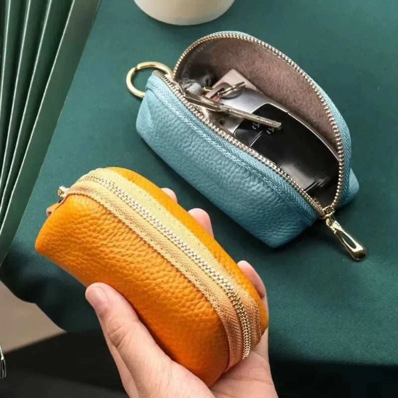 A hand holds an orange PU leather key organizer wallet next to a light blue zippered wallet on a green surface.