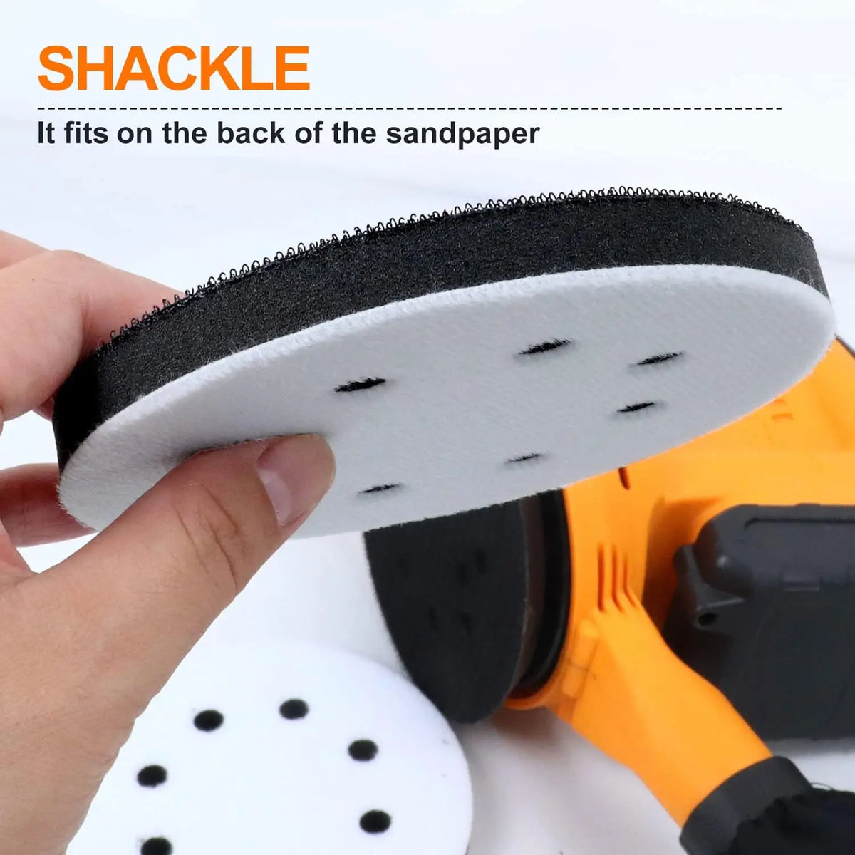 A hand is holding a black foam sanding pad that fits onto the back of an orange random orbit sander.