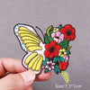 A hand holds an embroidered butterfly patch featuring yellow and white wings and a cluster of red and pink flowers.