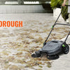 A person is using a black walk-behind push floor sweeper to clean a concrete area.