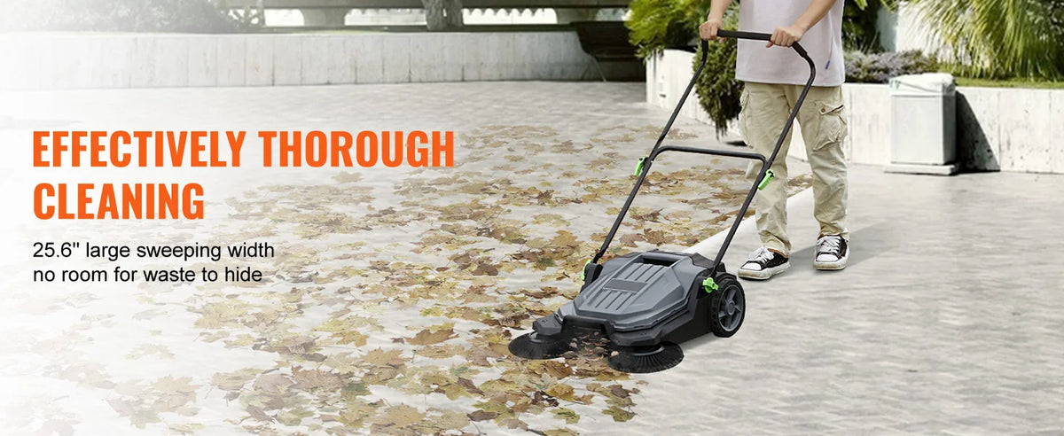 A person is using a black walk-behind push floor sweeper to clean a concrete area.