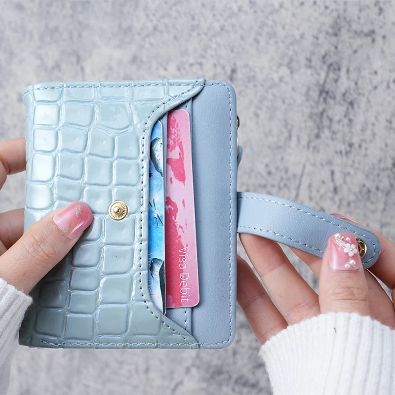 A hand holds a light blue crocodile-embossed clutch wallet with a pink card inserted.