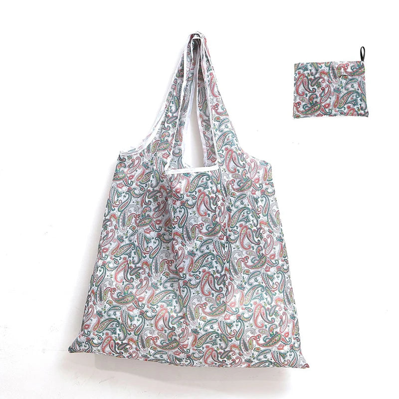 A reusable shopping tote bag featuring a floral pattern in shades of green, pink, and white, with an attached small carry pou