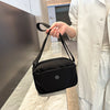A person holds a black nylon crossbody bag with a strap against a light marble surface.