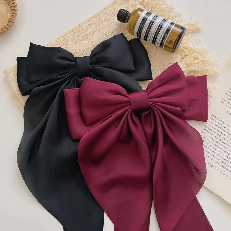 A set of silk bow hair clips in black and deep burgundy, with a glass bottle nearby.