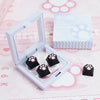 A white case containing black silicone cat paw keycaps and a box labeled Cat Claw Keycap for MX Switches on a pink background