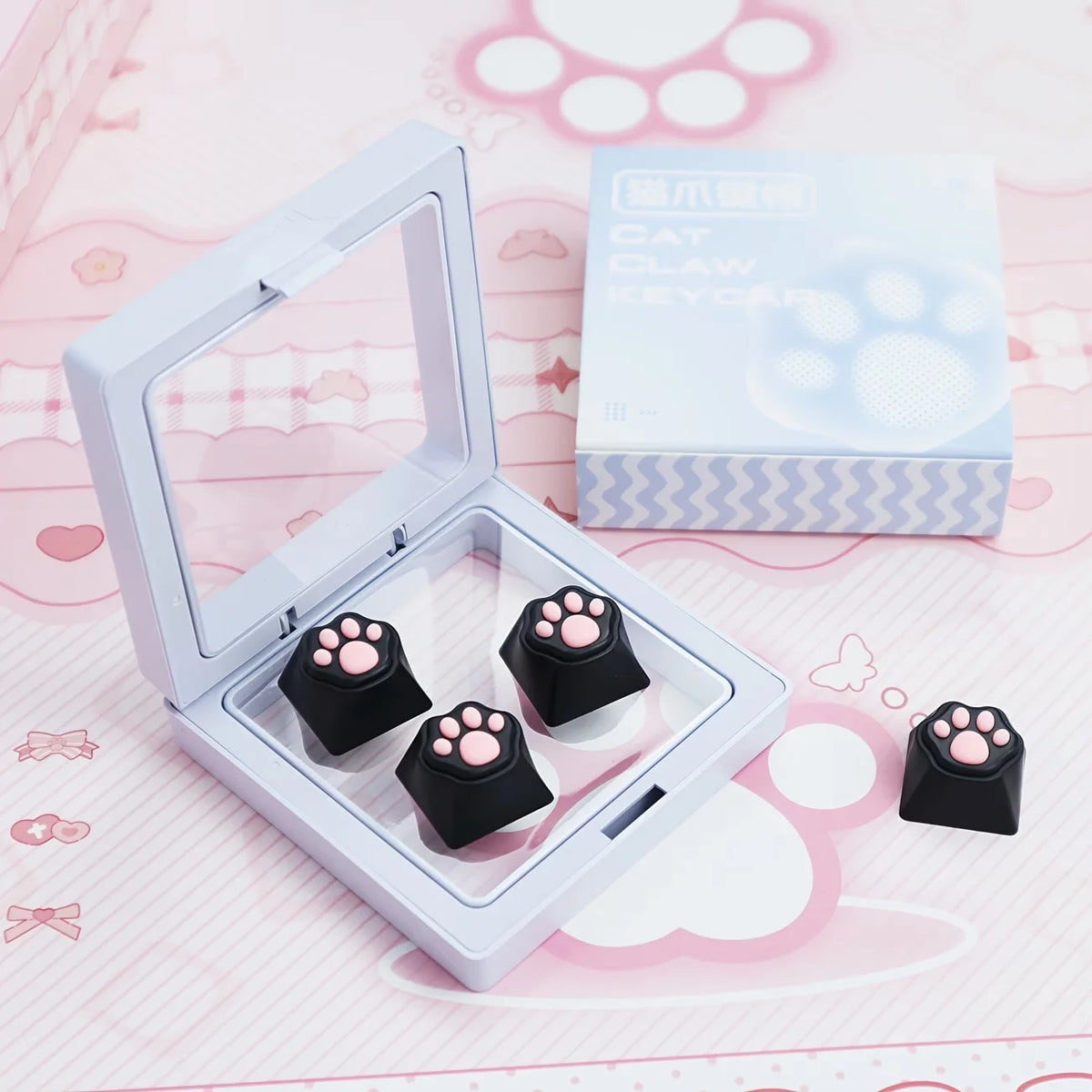A white case containing black silicone cat paw keycaps and a box labeled Cat Claw Keycap for MX Switches on a pink background