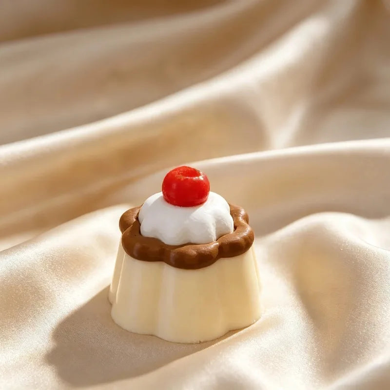 A small white cake with a chocolate ring and a red cherry on top resting on a beige fabric.