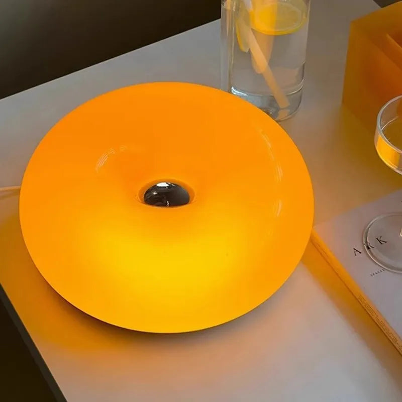 A bright orange circular LED light fixture resembling a donut is displayed on a white surface.