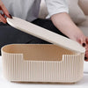 A hand opens a light beige cable management box organizer for power strips on a white surface.