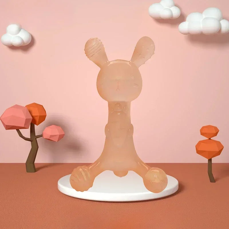 A light peach silicone cartoon rabbit teether standing on a white plate against a pink background with clouds and orange geom