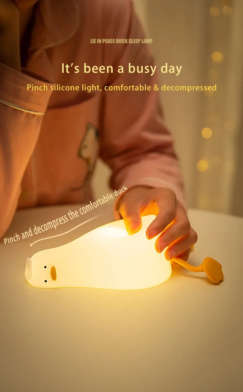 A hand is pinching a white silicone duck night light, illuminating the surface.