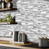 A kitchen backsplash featuring gray and white marble tile stickers above a wooden countertop.