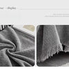 A close-up of a gray herringbone chenille sofa throw with tassel edges draped on a surface.