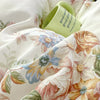 A close-up of a floral cotton pillowcase set featuring soft pink, yellow, and blue blooms with a light green tag.