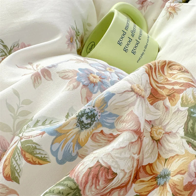 A close-up of a floral cotton pillowcase set featuring soft pink, yellow, and blue blooms with a light green tag.