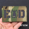 A rectangular camouflage patch with the letters EOD cut out in the center on a fabric background.