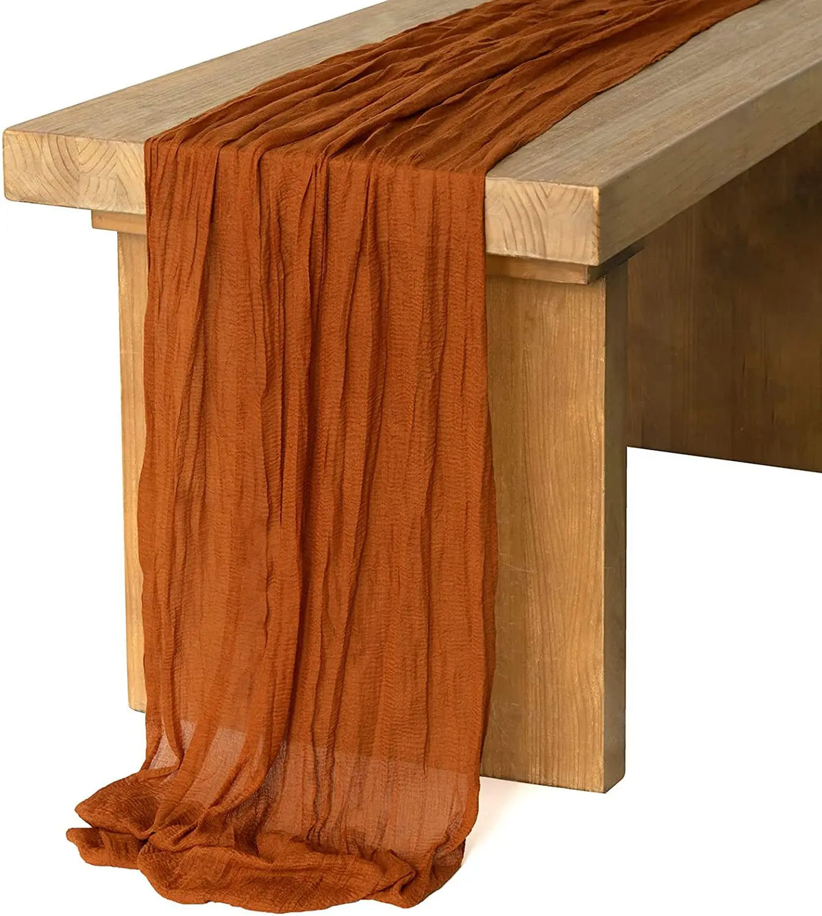 A rust orange cotton gauze table runner draped over a wooden table.