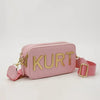 Pinkes Lederbeuteltasche mit goldenen Buchstaben KURT und passende Trageleiste.