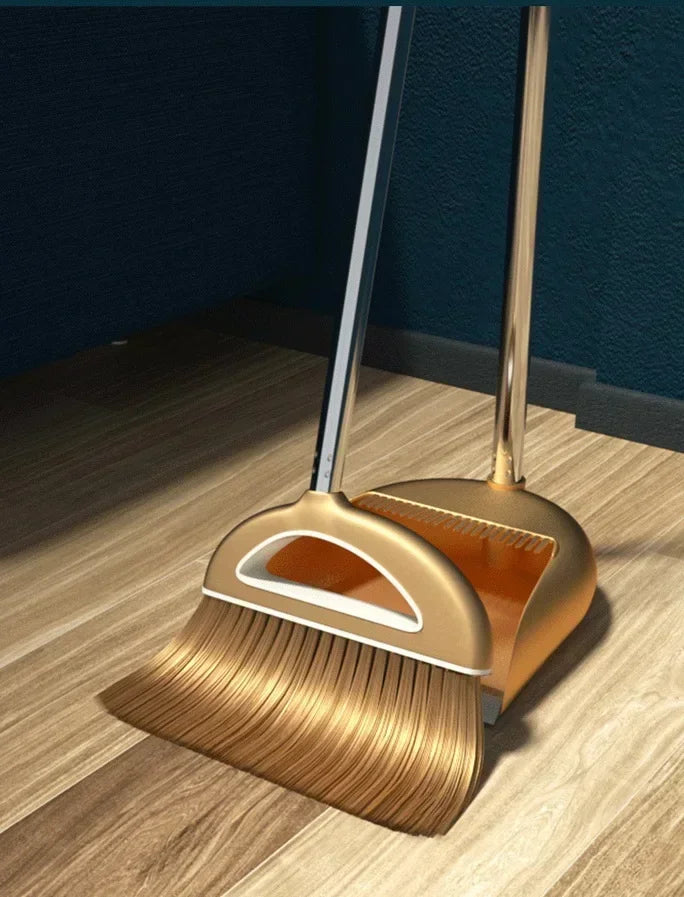 A golden broom and dustpan set with a floor wiper resting on a wooden floor.