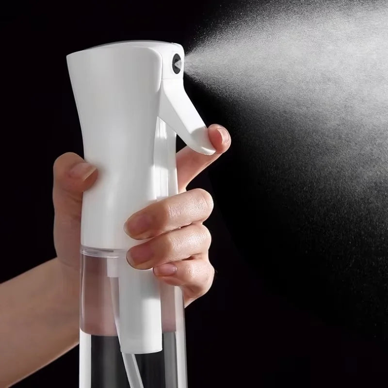 A hand is holding a white fine mist spray bottle and spraying a fine mist onto a dark surface.