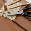 A pair of professional scalloped pinking shears rests on a wooden surface with pencils and patterned paper.