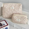 A beige floral quilted cosmetic bag with a light pink pattern is displayed on a white shelf.