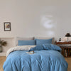A light blue quilted duvet cover set with matching pillowcases displayed on a bed against a white wall.