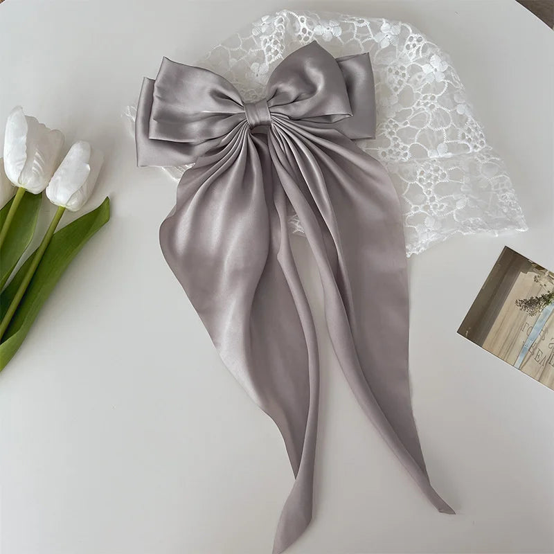 A silk gray bow tied in a large knot, resting on white lace fabric next to white tulips.