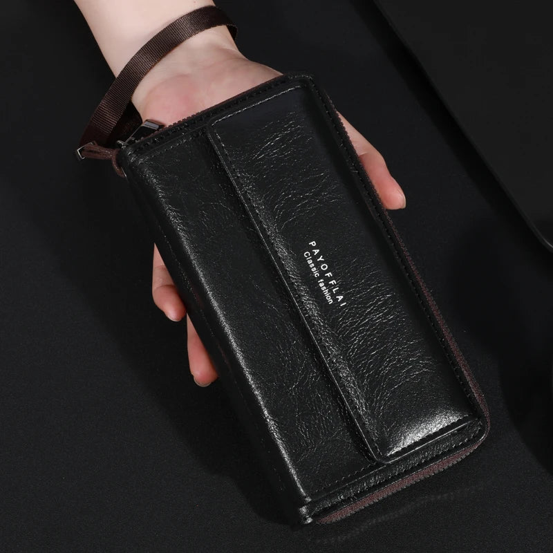 Une main tient un porte-monnaie clutch en cuir noir avec une sangle marron et du texte gravé.