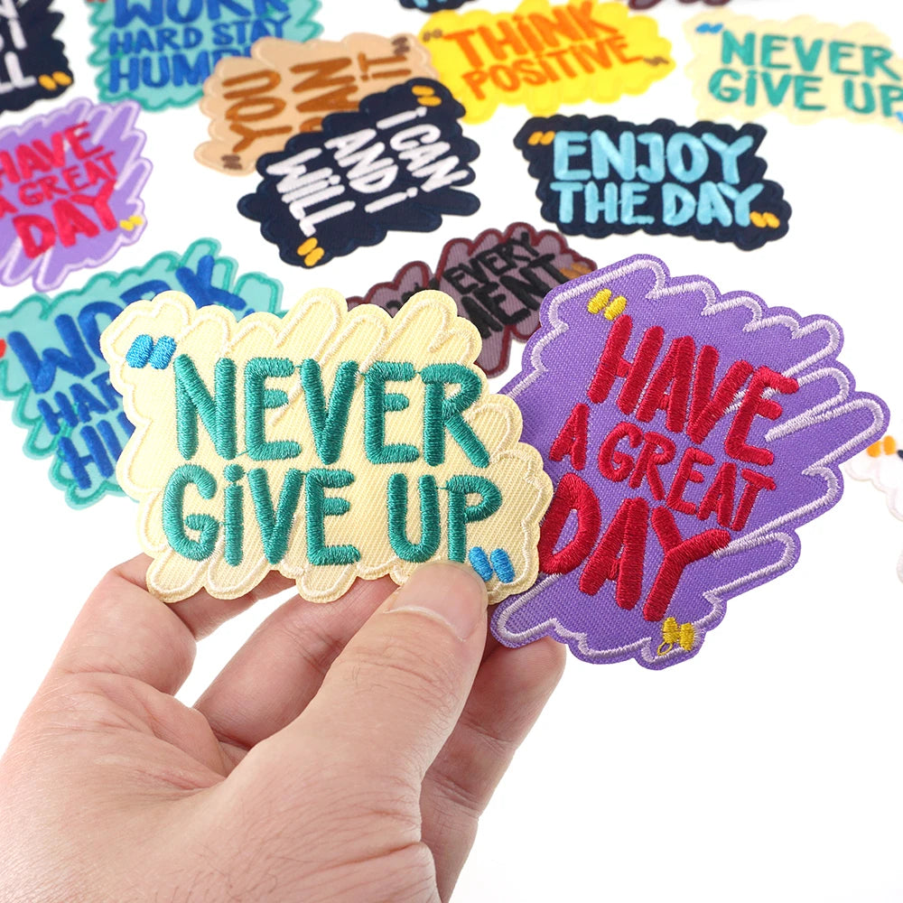 A hand holds a purple embroidered patch that says Have a Great Day