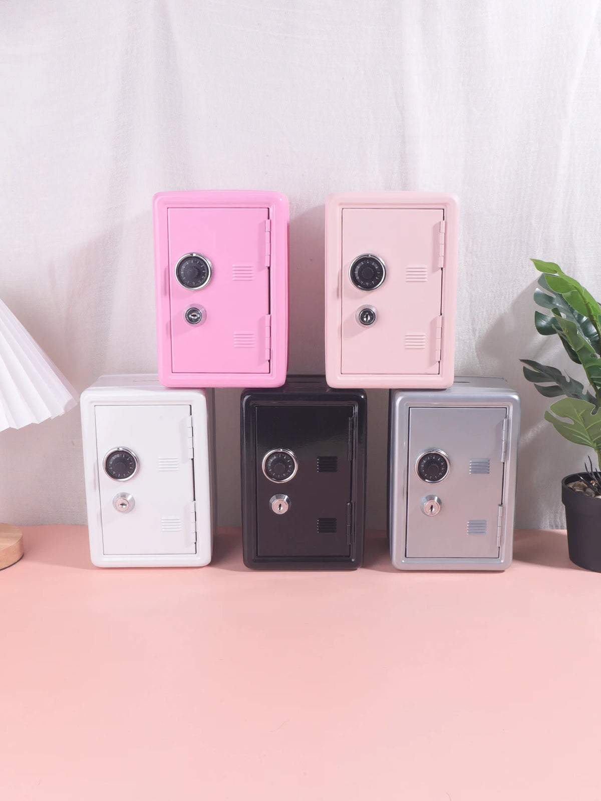 A collection of four vintage metal piggy banks in pink and gray colors displayed on a light pink surface.