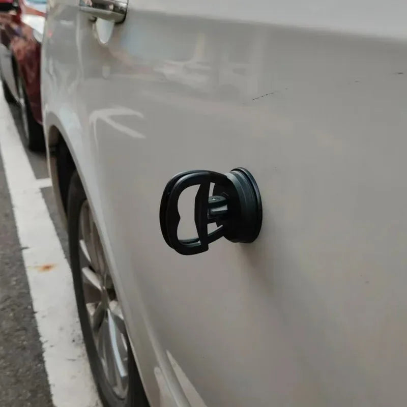 Close-up of a black car dent puller kit handle mounted on the side of a white car.