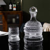 A clear crystal wine decanter with a decorative stopper and rotating aerator sits on a dark surface.