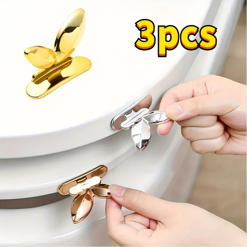 Three gold-colored touch-free toilet seat lifters with flush buttons being held by a hand.