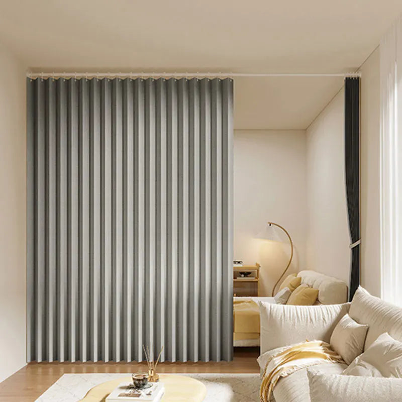 A modern gray pleated fabric room divider curtain standing in a bright, minimalist interior.