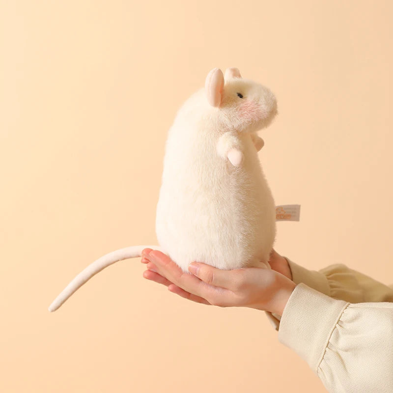 A small white plush mouse stuffed animal being held in a person's hand against a light beige background.