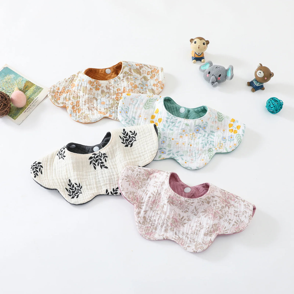 A collection of soft, patterned cotton baby feeding bibs and a small stuffed animal