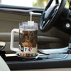 A silver insulated stainless steel tumbler with a white lid is placed on a car dashboard.
