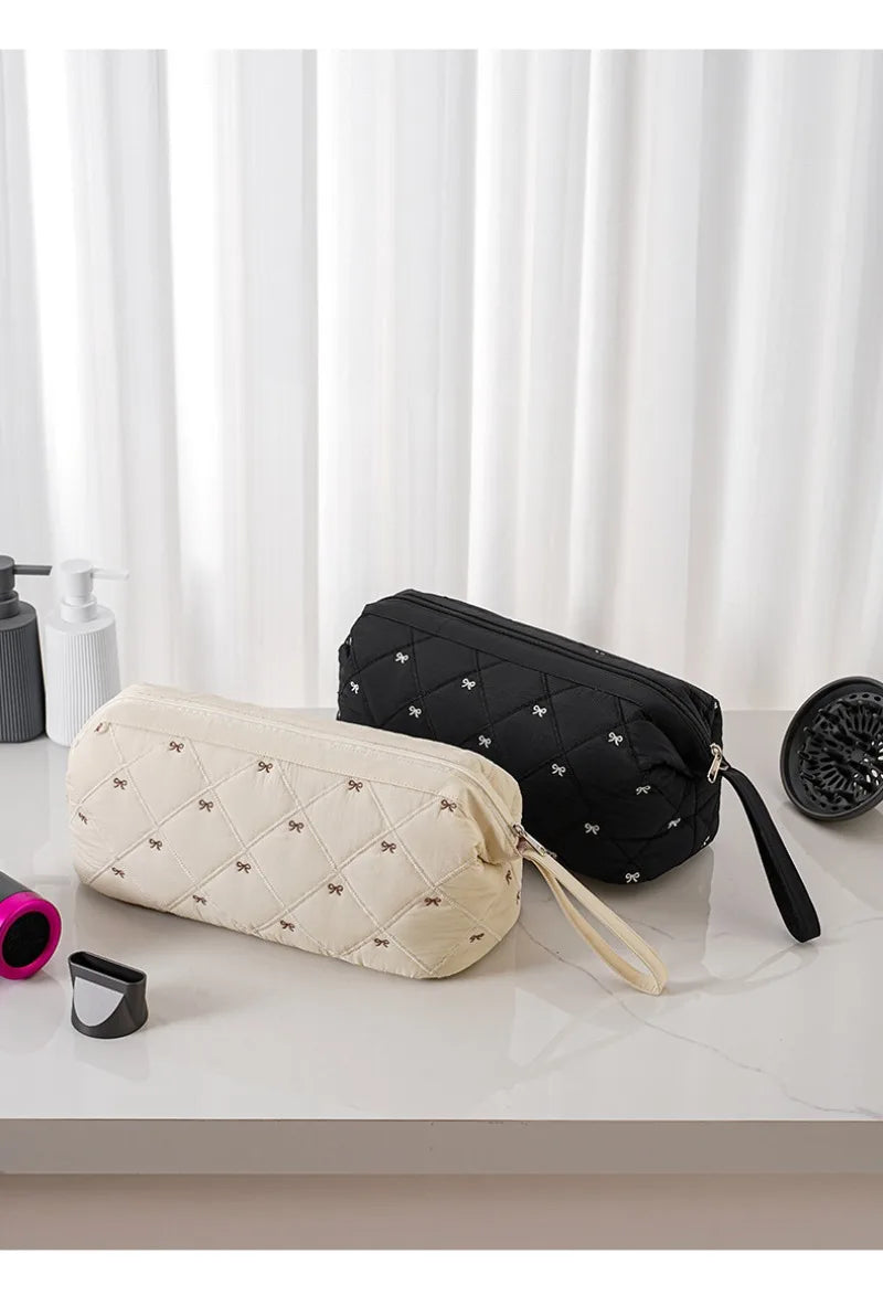 A beige quilted storage bag and a black quilted storage bag are displayed on a white surface.