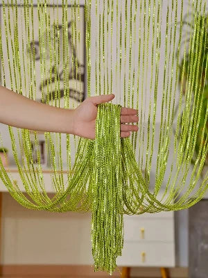 A hand is holding a vertical curtain made of long, shimmering lime green tassels hanging in the air.