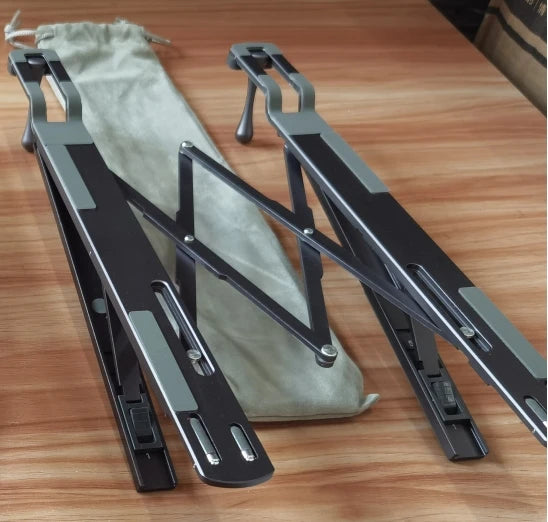 A pair of black foldable aluminum laptop stands are shown resting on a wooden surface.