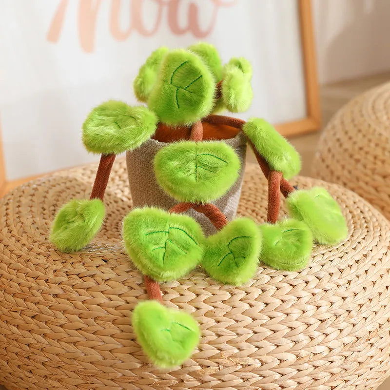 A lifelike plush potted plant with soft green leaves and brown stems sitting on a woven surface.