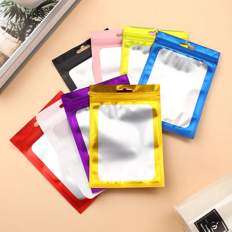 A collection of colorful Mylar ziplock bags with clear windows for jewelry and small item packaging arranged on a light backg