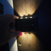 A hand is activating a solar powered outdoor wall light, illuminating the textured surface with warm light.