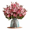 A bouquet of pink cherry blossoms arranged in a teal ceramic vase on a wooden coaster.