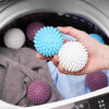 A hand is holding a cluster of light blue and white reusable laundry balls inside a washing machine drum.