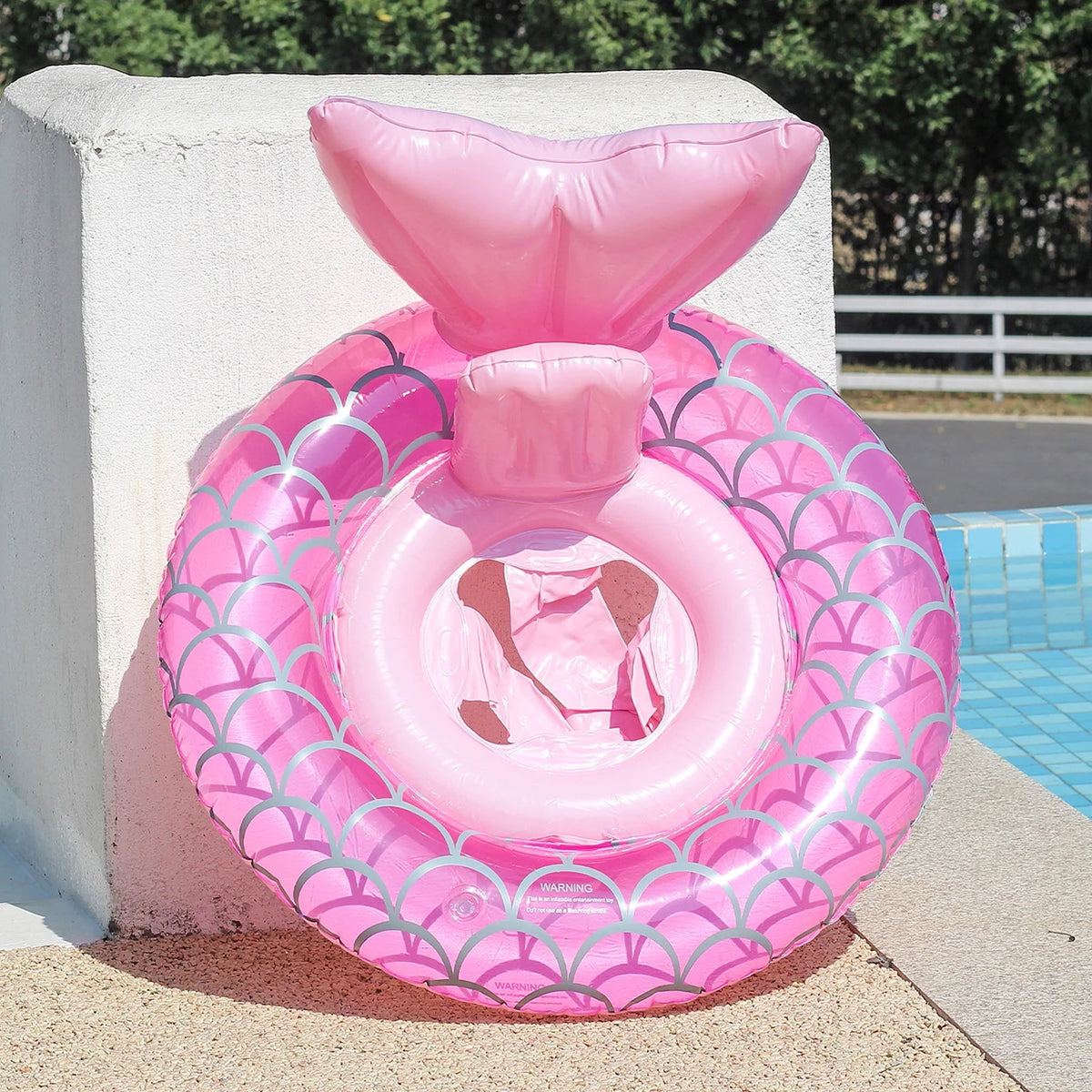 A pink inflatable swim ring shaped like a stylized heart is resting on a concrete ledge next to a swimming pool.